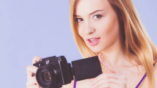 摄影师女孩拍摄的图像。蓝色背景的可爱的金发女郎带摄像头的女人
