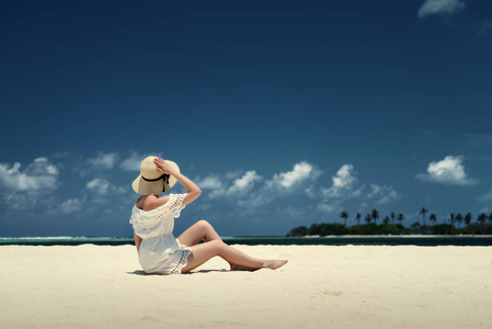 一个女孩在一顶帽子，坐在沙滩上。马尔代夫。白色沙滩