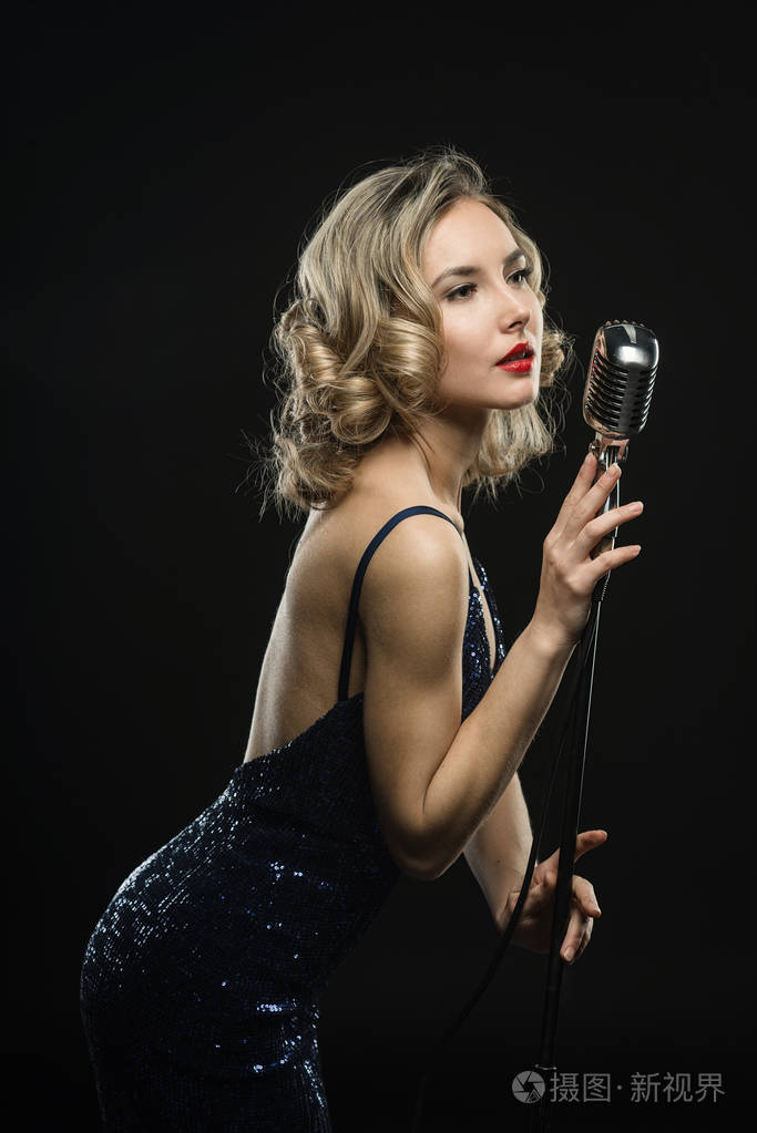 性感的年轻女孩歌手唱与银色复古麦克风在黑色背景