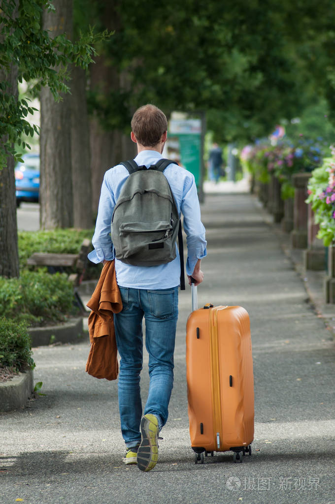 男子步行在街上与手提箱和背包从火车站