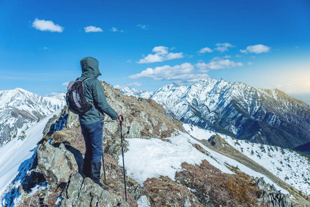 徒步旅行的男子徒步旅行者站在白雪皑皑的山脚下的山顶, 在晴朗的天气。旅游理念与实现目标