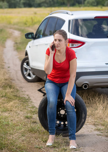 心烦的年轻妇女得到了她的汽车轮胎刺穿和呼叫汽车服务帮助