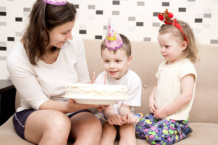 蛋糕生日的孩子。妈妈为孩子过生日举行生日蛋糕。节日帽和蜡烛蛋糕的母亲和孩子们