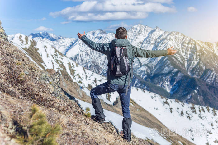 男性徒步旅行者庆祝成功站在山顶上, 在一座雪山的山顶上, 在一个晴朗