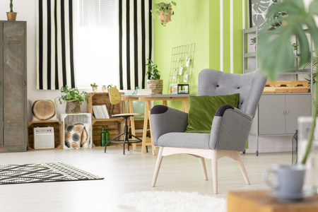 绿色枕头在灰色扶手椅在现代客厅内部与条纹窗帘。真实照片