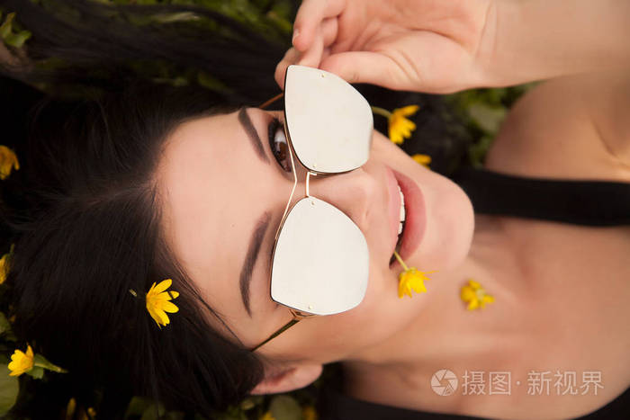 年轻漂亮的黑发女郎，在夏天，花黄色躺在草地上的银镜太阳镜