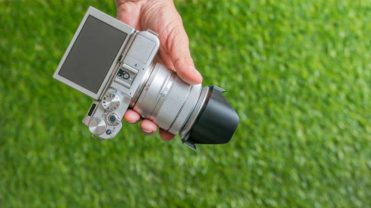 手持照相机的手, 在绿色草地背景上手持相机的摄影师手特写。特写, 选择性聚焦