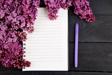 树枝上的春天花花束盛开的丁香在黑色的桌子上。女日记笔记本。花的创意设计。平躺。文本位置