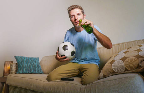 年轻的有吸引力和紧张的人集中看足球比赛在电视举行啤酒瓶和足球在压力下兴奋地享受沙发沙发上的比赛支持者概念