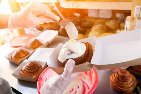 一个女面包师的特写在保护手套准备包子 cinnapons 和倒奶油对他们在面包店