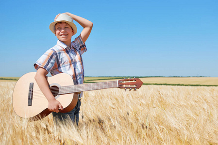 儿童男孩与吉他是在黄色麦田, 明亮的太阳, 夏天风景