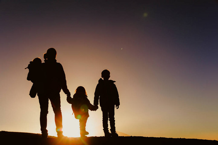 母亲带着两个孩子徒步旅行在日落时的剪影照片