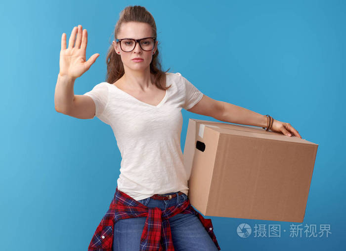 白色衬衣的年轻妇女与一个纸板盒显示停止手势隔离在蓝色背景上