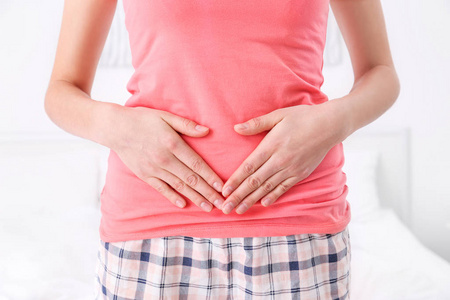 年轻的女人,手放在她的肚子在家里,特写照片