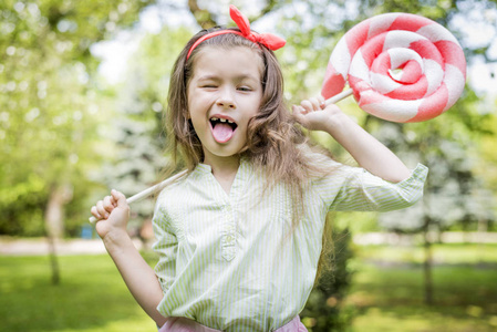 年轻的女孩拿着大的彩色棒糖。夏日快乐的童年观念。滑稽的女孩
