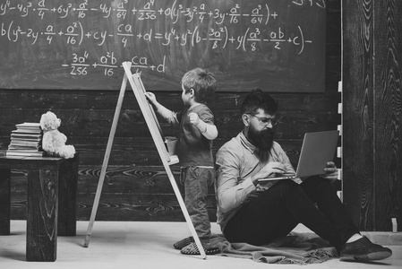 数学课。算术课在学校。孩子在黑板上写字, 而集中的老师在笔记本电脑上工作。侧面观看坐的人和站立的孩子回到后面