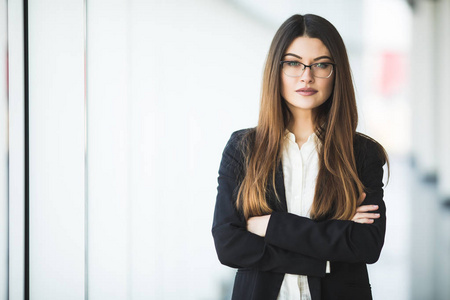 微笑的年轻商业女人交叉的双臂，站在办公室提起