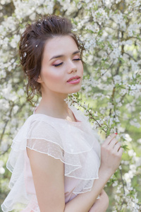 美丽的温柔甜美的女孩, 在一个阳光明媚的春天, 在粉红色的礼服, 在盛开的树的发型附近