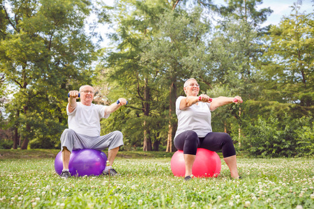 微笑的资深男人和妇女做健身运动在公园健身球