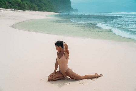 迷人的女孩与的身体是从事健身在白色沙滩上。穿着泳装的年轻妇女在国外的暑假里晒日光浴。沙漠岛上的迷人模特