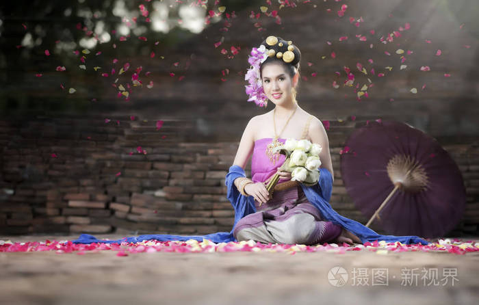 穿着泰国传统服饰的年轻美女捧着莲花坐在老砖庙里