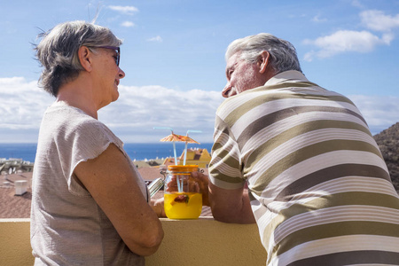 微笑着老妇人和男人, 在屋顶的 sumer 太阳下的水果鸡尾酒。蓝晴天空海景