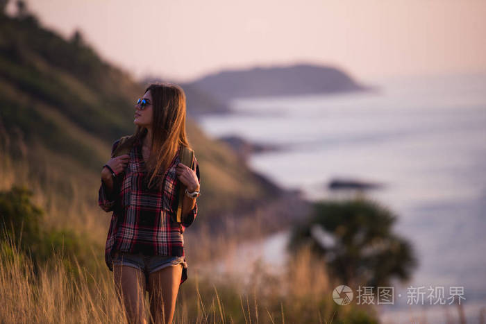 夏天阳光灿烂的生活方式时尚肖像的年轻时尚时髦女人走在山上，穿着可爱时髦的打扮，微笑享受周末，背包旅行。令人敬畏的海洋观