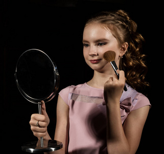 小女孩与圆镜子做化妆在黑暗的背景上