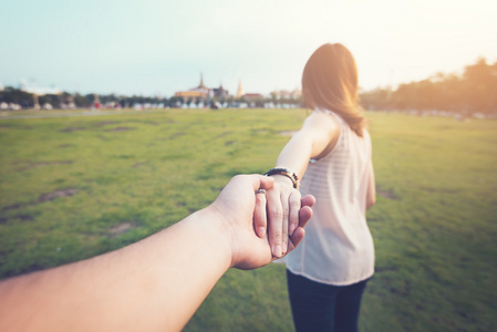 年轻女子在绿地上握着男人的手。把重点放在手上。夫妇在旅游概念