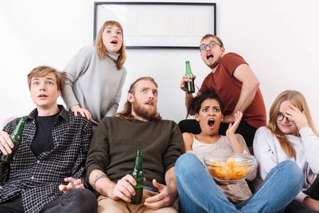 一群害怕的朋友坐在沙发上, 看恐怖电影一起在家里的筹码和啤酒