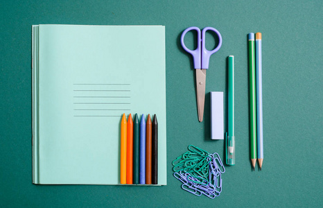 一套学校用品, 配有笔记本钢笔铅笔剪刀和夹子。学校用品, 彩色铅笔的绿色背景。剪刀和罗盘, 蓝色的尺子。复制空间