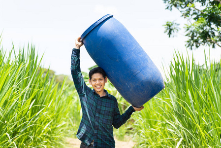 亚洲青年农民携带蓝水箱 发酵水箱 浇灌草田