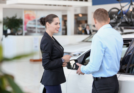 在汽车经销店与客户合作的年轻女售货员照片