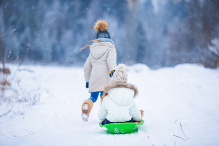 可爱的小女孩享受驾雪橇。滑雪橇的孩子。在雪中，孩子们在户外玩。在圣诞前夕户外家庭度假