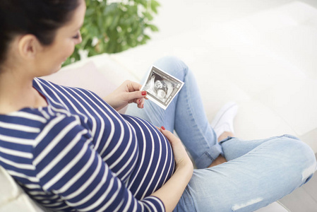 高角度拍摄的快乐怀孕妇女手持手3d 超声图像她的宝宝, 而在沙发上放松