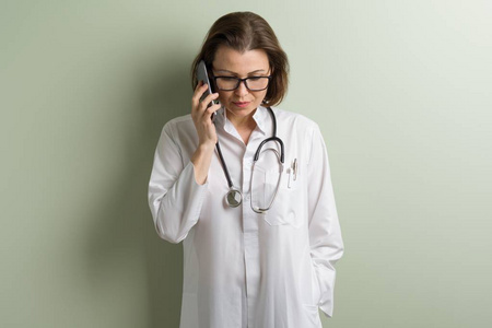 积极的医生女人说手机。背景绿色墙壁在诊所里