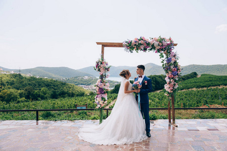 新婚夫妇相爱看着对方, 享受婚礼的日子。他们站在一个粉红色, 白色和蓝色的花朵拱