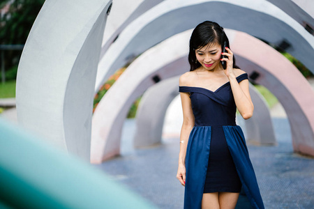 一个时尚的亚洲妇女的肖像在公园的蓝色礼服与智能手机