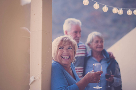 晚上在阳台上的休闲的老年妇女的大微笑。喝点酒, 和朋友在聚会上玩得开心