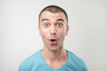 惊讶的年轻男子在马球 t恤上灰色背景.特写面部表情照片