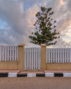 公共公园的日出时, 白色风化的木制庭院门和围墙, 背景为单棵树和多云