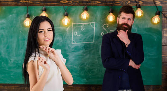 男子与胡子和年轻女士教师站在教室, 黑板上的背景。女士老师和大胡子的时髦的校长在学校一起工作。世代概念