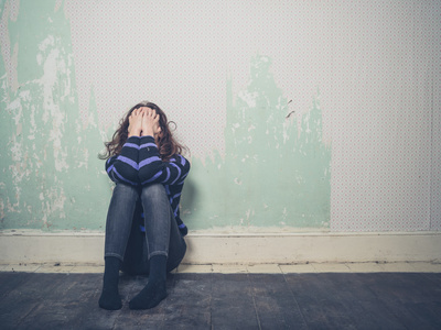 忧郁的年轻女子坐在空荡荡的房间地板上照片