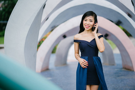 一个时尚的亚洲妇女的肖像在公园的蓝色礼服与智能手机