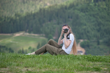 女孩与照相机坐在山和相片。背景林