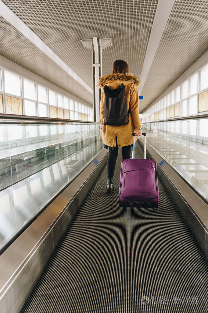 在自动人行道上国际航空手提行李的年轻女子