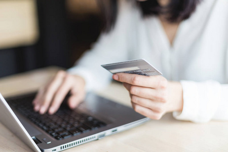 一个戴眼镜的年轻女商人坐在咖啡馆里, 拿着笔记本电脑, 拿着一张信用卡在网上购物。网上购物的概念