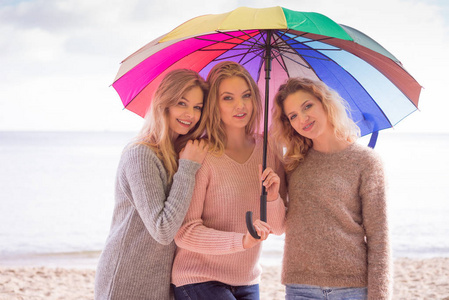 三美丽的年轻女性朋友下五颜六色的雨伞阳伞。时尚女性穿毛衣花时间户外