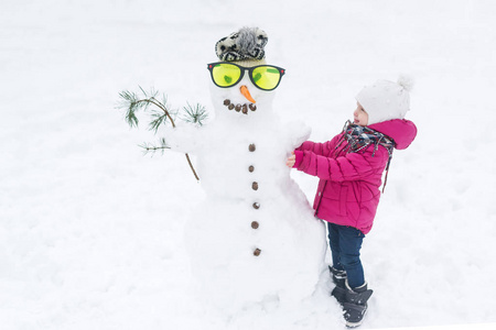 快乐的女孩 plaing 与一个雪人的玻璃在一个下雪的冬天散步