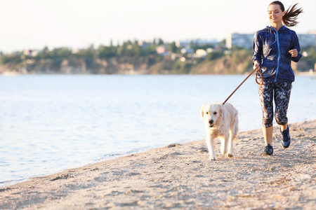 在海滩上与她的狗一起的年轻妇女。宠物护理